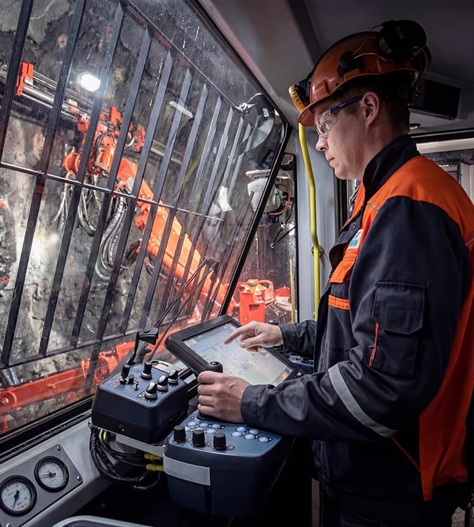 Industrial touchscreen panel operator using wireless remote control system to monitor heavy-duty mining equipment in extreme environment, demonstrating durability and reliability of industrial-grade displays